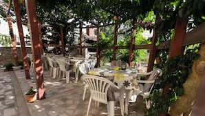 An outdoor patio with white plastic chairs and tables, surrounded by greenery and a pergola structure. - Close To The Sea, 1-bedroom Apartment Sonia (Kukljica)
