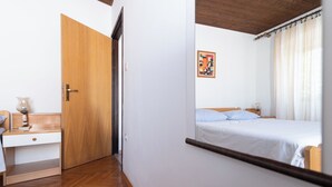 A bedroom with a wooden door, a bedside table with a lamp, a bed with white linens, and a framed picture on the wall. - Close To The Sea, 1-bedroom Apartment Sonia (Kukljica)
