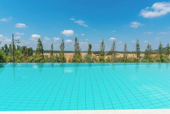 Une piscine dont le fond est recouvert de carrelage, entourée d’arbres et surplombée par un ciel dégagé.
