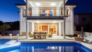 Ein zweistöckiges Haus mit Swimmingpool, Sitzgelegenheiten im Freien und einem Balkon.