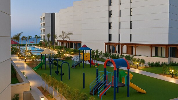 A playground with slides and climbing structures, surrounded by a landscaped area with trees and a pool in the background. - Serene Chalet Retreat in Port Said Governorate (Al-Manasrah)