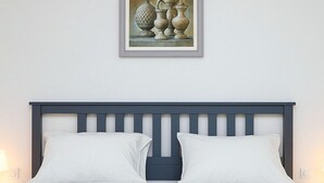 A bed with a dark headboard, white pillows, and a blue patterned bedspread. Above the bed, there is a framed picture of pottery. - Chalet Porto Said Tourist Resort (Al-Manasrah)