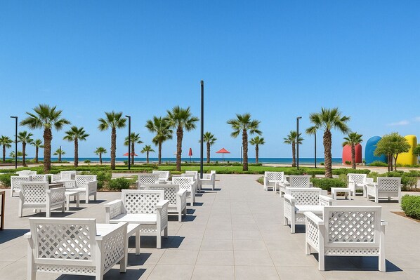 A beachside patio with white outdoor furniture, palm trees, and a clear view of the ocean.