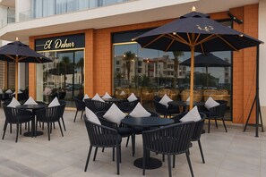 An outdoor seating area with tables and chairs, umbrellas, and a building with a sign reading 'El Dah'.