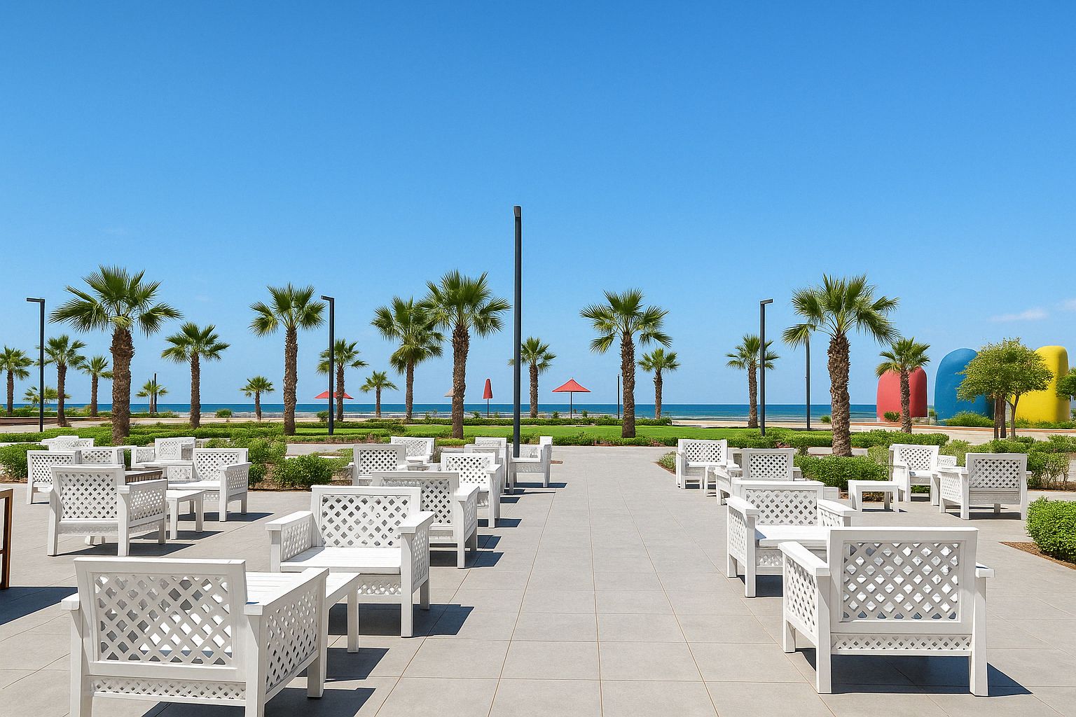 A beachside patio with white outdoor furniture, palm trees, and a clear view of the ocean.