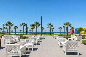 A beachside patio with white outdoor furniture, palm trees, and a clear view of the ocean.