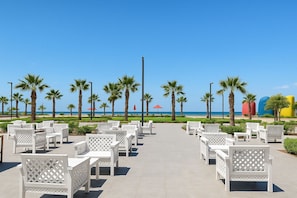 A beachside patio with white outdoor furniture, palm trees, and a clear view of the ocean.