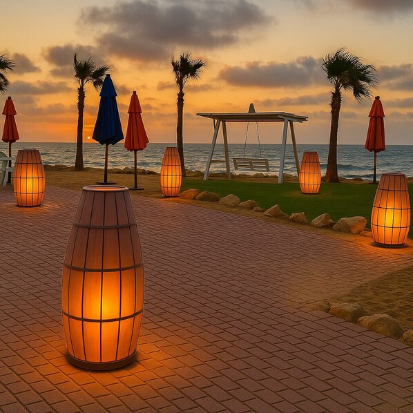 A beachside walkway with palm trees, outdoor seating, and illuminated lanterns.