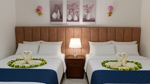 A hotel room with two beds, each with a heart-shaped towel and sunflowers. There are wall-mounted lamps and framed pictures above the beds. - Spacious Beach Hideaway (Al-Manasrah)