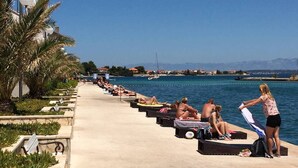 A seaside promenade with sun loungers and palm trees. - Beachfront Holiday House Žal (Preko)