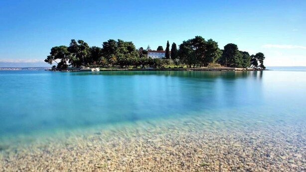 A clear view of a pebble beach leading to a small island with trees and a building. - Beachfront Holiday House Žal (Preko)