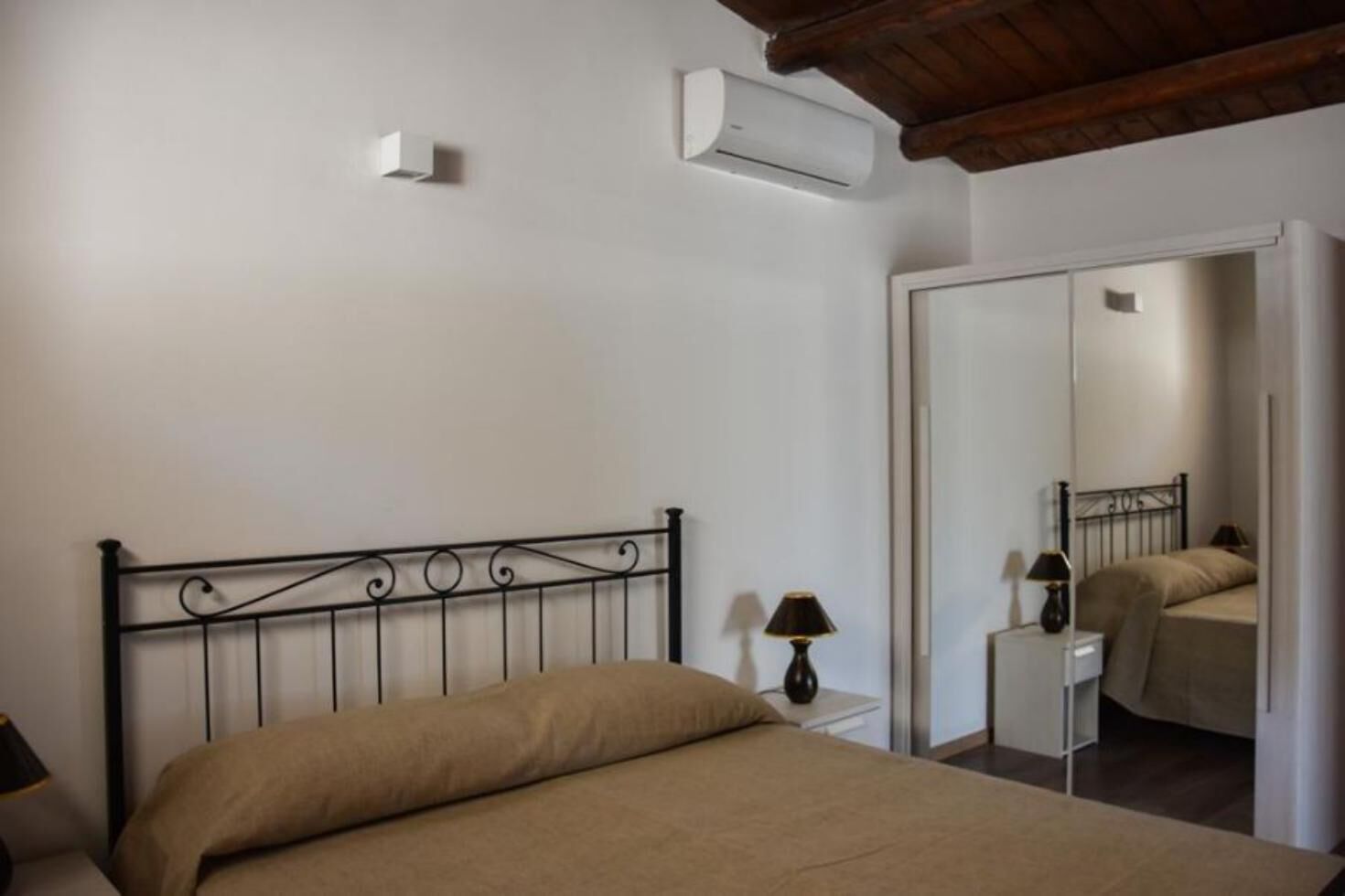 Un dormitorio con cama, mesita de noche con lámpara, unidad de aire acondicionado y espejo.