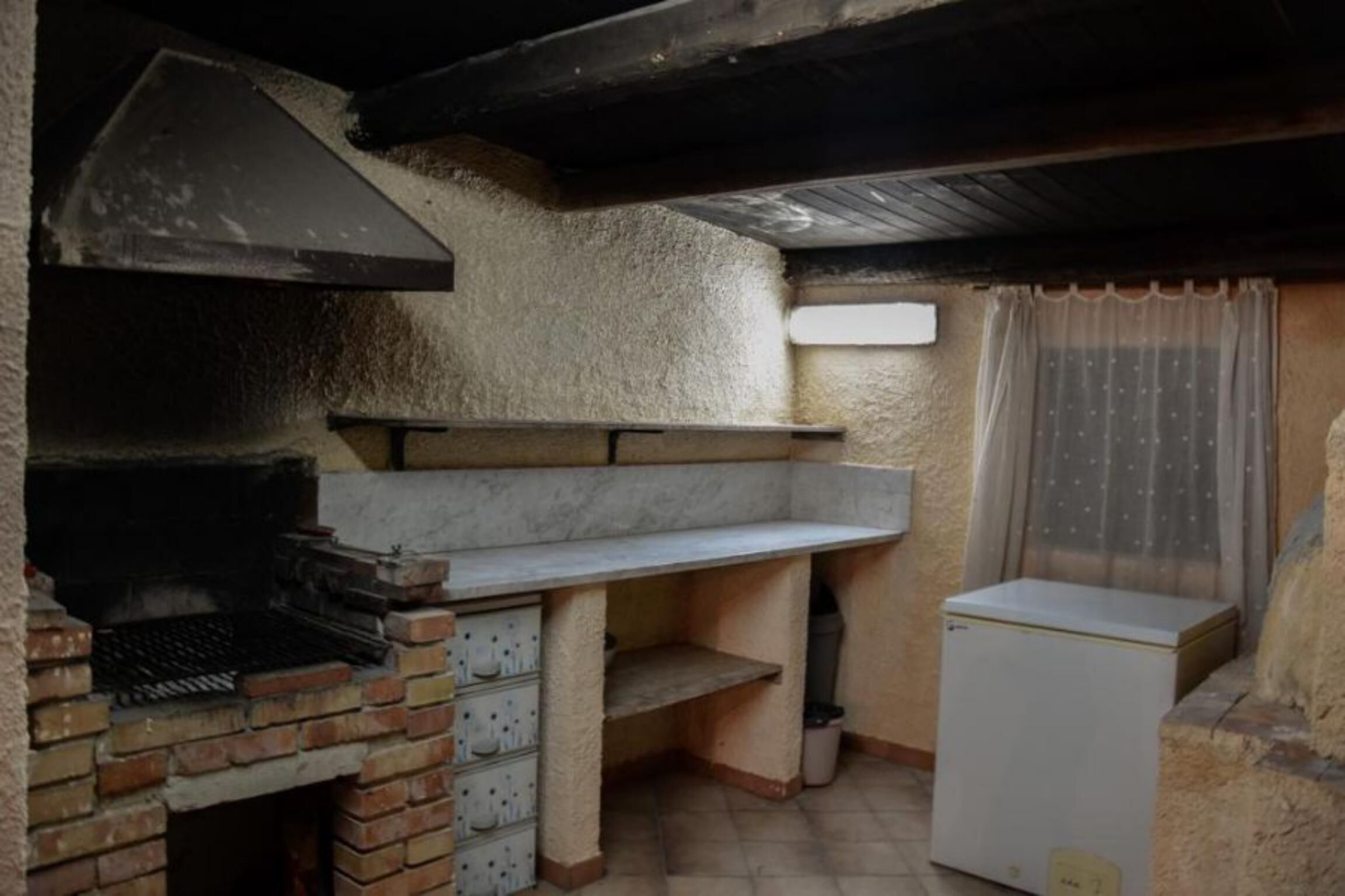 Eine kompakte Küche mit Backofen, kleinem Kühlschrank und einem Fenster mit Vorhang.