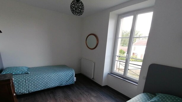 A room with two beds, a window, a radiator, and a circular light fixture. - Gîte de la Gare (Esclavolles-Lurey)