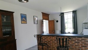 A kitchen with a brick backsplash, two bar stools, a wooden cabinet, and a window with curtains. - Gîte de la Gare (Esclavolles-Lurey)