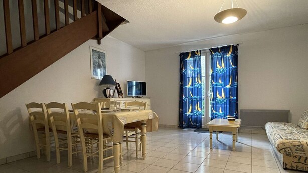 A dining area with a wooden table and chairs, a TV, and a lamp.