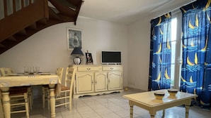 A dining area with a table, chairs, a cabinet, a television, and a patterned curtain.