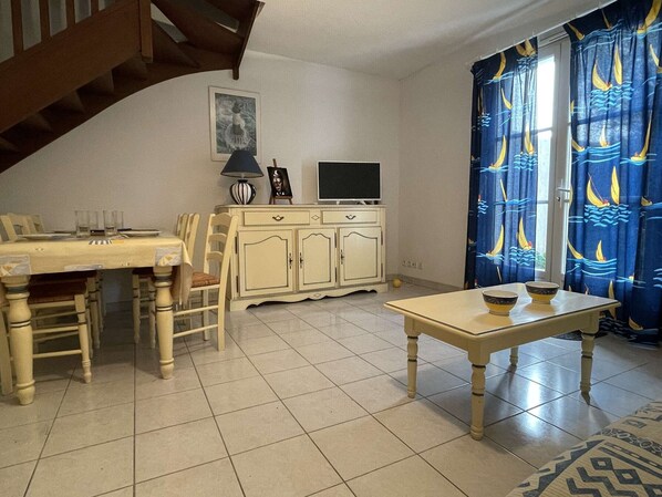 Un'area pranzo con tavolo, sedie, un mobile, una televisione e una tenda decorata.