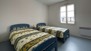 A bedroom with two single beds, a window, a ceiling fan, and a radiator.