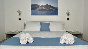 A neatly made bed with rolled towels, a blue accent pillow, and a framed picture of a coastal landscape on the wall. - Family villa with pool (Campania)