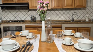 A kitchen with wooden cabinets, a tiled backsplash, and a dining table set with white dishes, glasses, and a vase with flowers. - Family villa with pool (Campania)