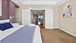 A hotel room with a large bed, a nightstand, a painting, and a view into the kitchen area.