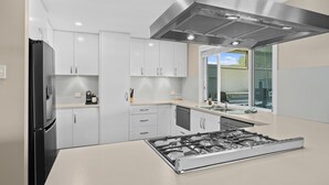 A modern kitchen with white cabinets, a black refrigerator, a stainless steel range hood, and a window with a view of greenery.
