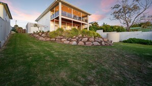 A modern two-story house with a balcony, a well-maintained lawn, and a stone retaining wall.