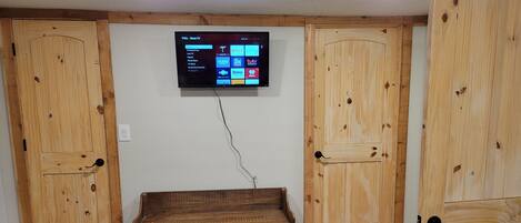 Une pièce avec un coffre en bois, un téléviseur fixé au mur diffusant des services de streaming et des portes en bois.