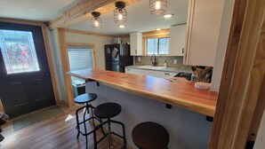 A kitchen with a wooden countertop, two stools, a refrigerator, and a window with blinds. - Cabin on a Secluded Cove -- READ DESCRIPTION REGARDING SAM RAYBURN WATER LEVEL (Broaddus)