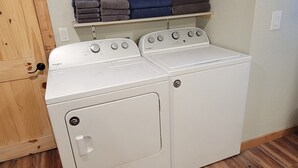 A laundry room with a washer and dryer, wooden flooring, and a cabinet above the appliances. - Cabin on a Secluded Cove -- READ DESCRIPTION REGARDING SAM RAYBURN WATER LEVEL (Broaddus)