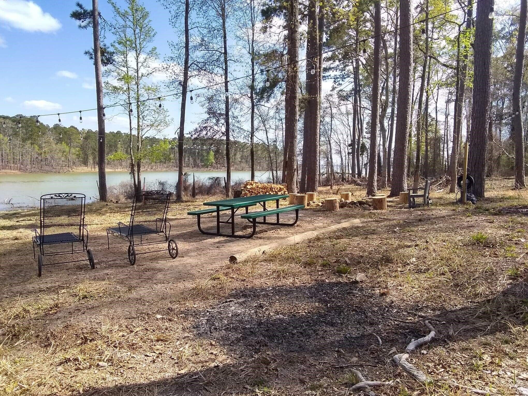 A campsite with picnic tables, chairs, and a view of a lake surrounded by trees.