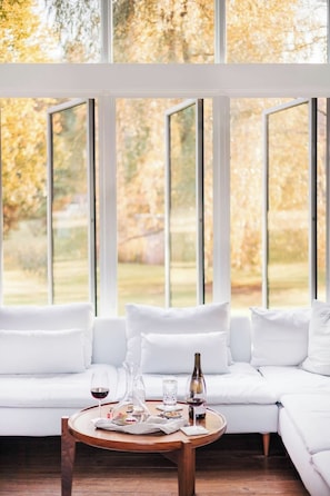 Un intérieur moderne avec un canapé blanc, une table basse en bois et de grandes fenêtres donnant sur la verdure.