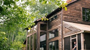 A modern wooden cabin with large windows, a covered porch, and a person entering. - Glasco Woodstock - 16 Acres with Mountain View. (Saugerties)