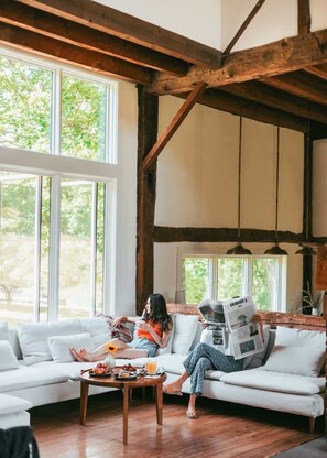 A room with a wooden ceiling, large windows, a white sofa, and a coffee table with food and drinks. - Glasco Woodstock - 16 Acres with Mountain View. (Saugerties)