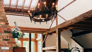 A spacious living area with a high ceiling, exposed wooden beams, a chandelier, a white sofa, a patterned rug, and a brick wall. - Glasco Woodstock - 16 Acres with Mountain View. (Saugerties)