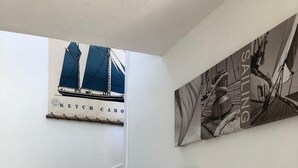 A staircase with wooden steps and a white wall. There are three framed pictures on the wall: one of a sailboat, one of a ship's wheel, and one of a ship's rigging. - House fig trees Roch Priol (Quiberon)