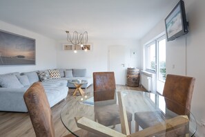 A modern living room with a glass-top coffee table, a sofa, and two brown chairs. - Ostenfelder Stuuv vacation apartment in Ostenfeld for up to 3 people (Ostenfeld)