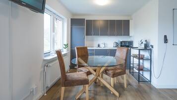 Een moderne keuken met een ronde glazen tafel en bruine gestoffeerde stoelen, een inbouwoven en een magnetron.