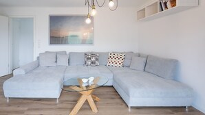 Ein modernes Wohnzimmer mit einem grauen Ecksofa, einem Glastisch und einer Pendelleuchte.