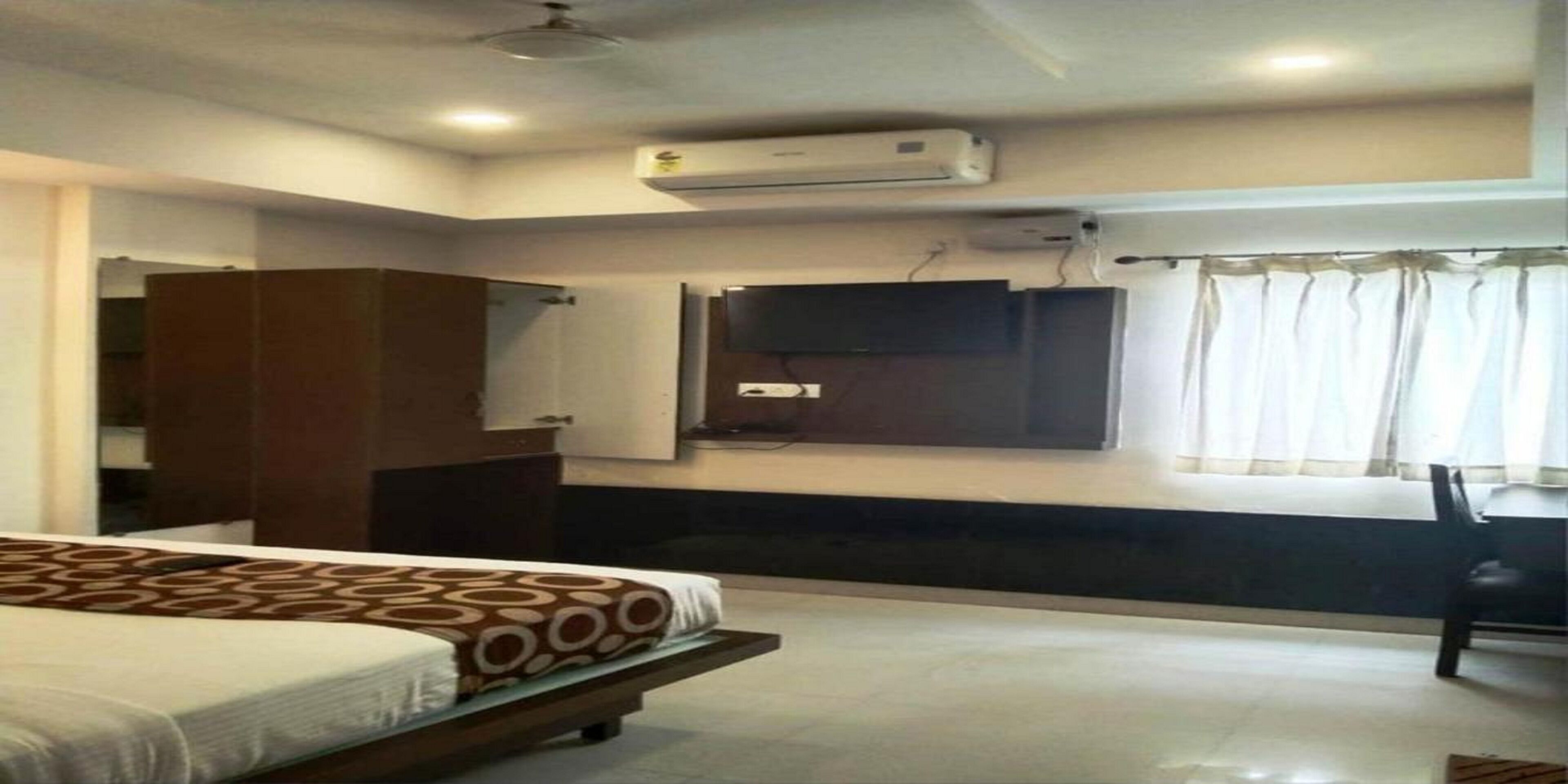 A hotel room with a bed, wardrobe, TV, and air conditioning unit.