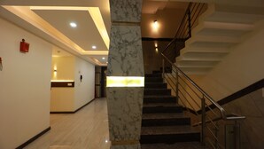 Un hall d’hôtel moderne avec un sol en marbre, une colonne centrale et un escalier doté de rampes en métal.