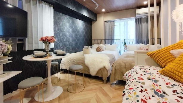 A modern bedroom with a bed, bedside tables, a small sitting area, and a TV. - 4 min walk from the nearest station in the most prosperous town in Shinjuku City Apartment room (新宿区)