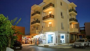 A multi-story hotel with balconies, a ground-level shop, and parked cars. - Helen Suites (Hersonissos)