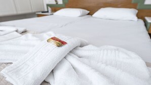 A neatly made bed with white linens and a folded towel on the side. - Helen Suites (Hersonissos)