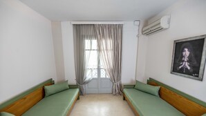A room with two green upholstered benches along the walls, a window with sheer curtains, and a framed picture on the wall. - Helen Suites (Hersonissos)