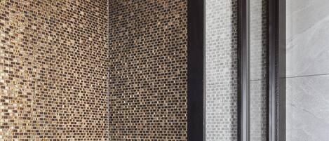 A modern shower with mosaic tile walls and a glass enclosure.