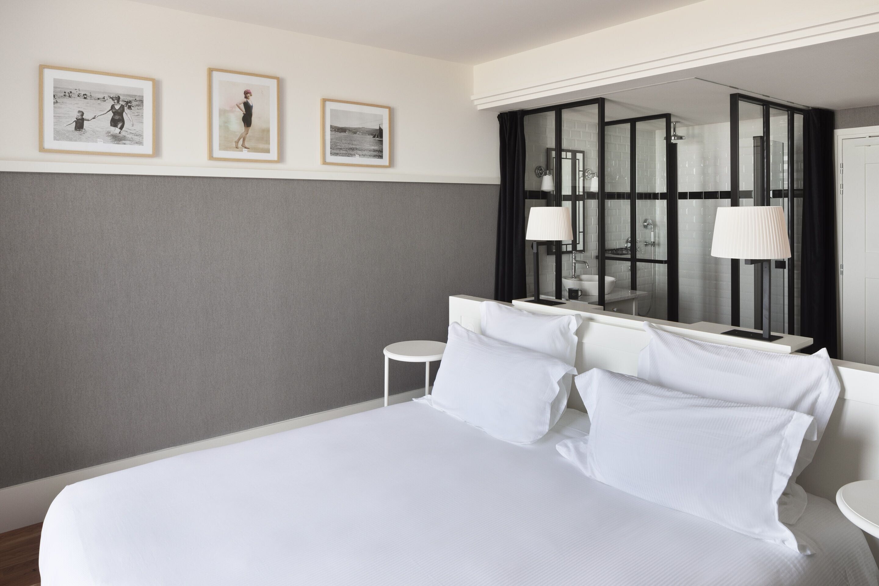 Ein Hotelzimmer mit einem großen Bett, einem kleinen runden Tisch, einem Spiegel und drei gerahmten Bildern an der Wand.