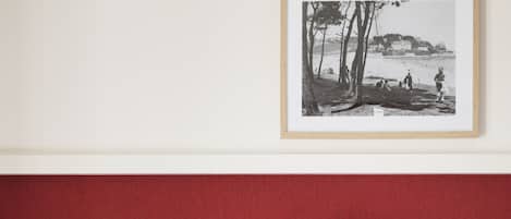 A bedroom with a red accent wall, a white bedside table, a lamp, and a framed picture on the wall.