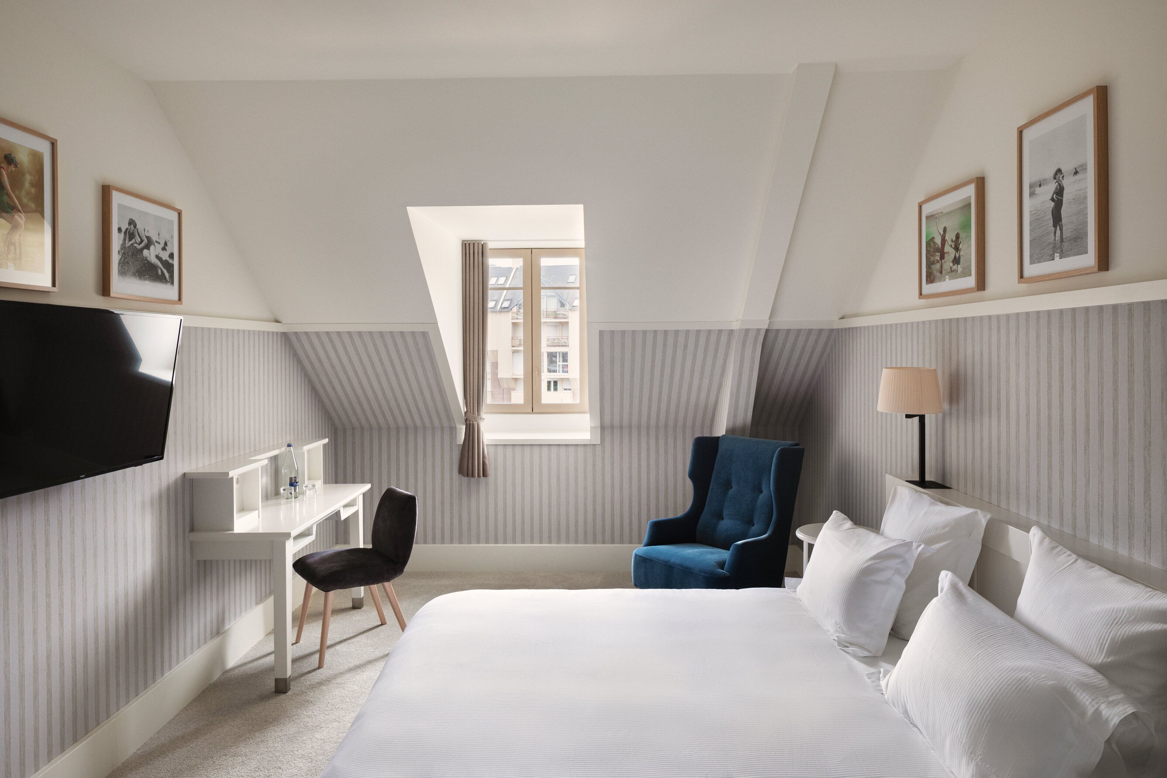 Ein Hotelzimmer mit einem Bett, einem Schreibtisch, einem Sessel, einem Fernseher und einem Fenster mit Vorhängen.